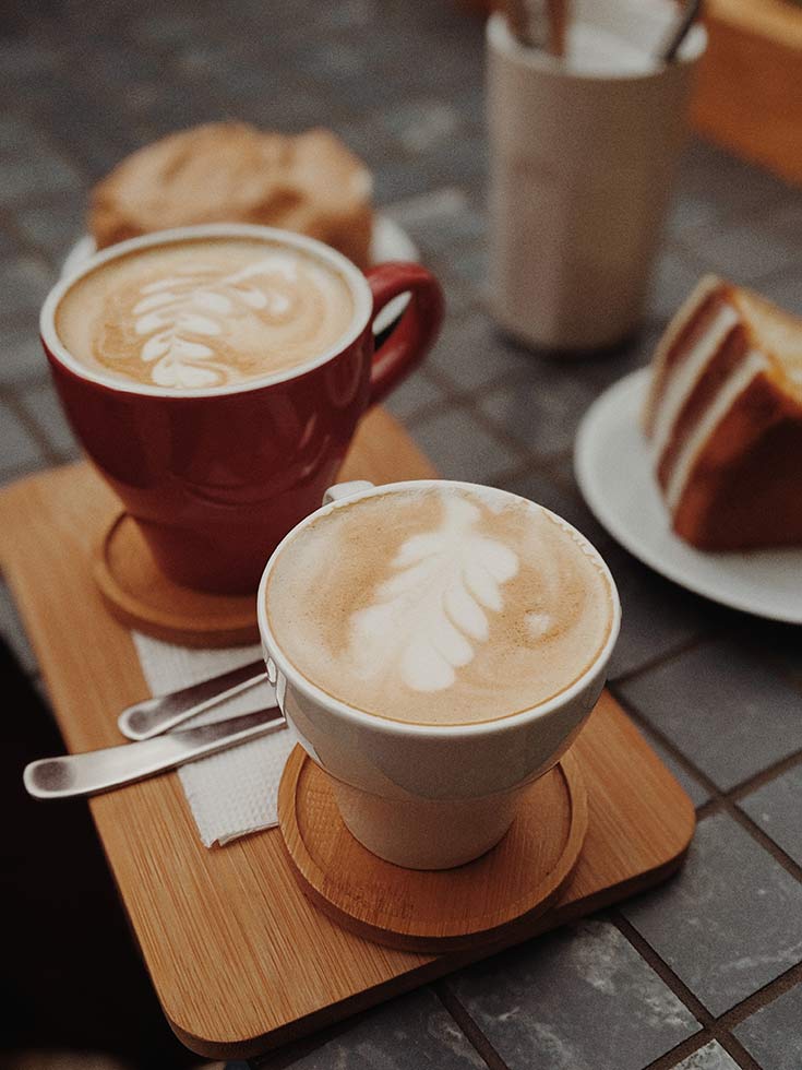 Two lattes sit on wooden saucers on a table.