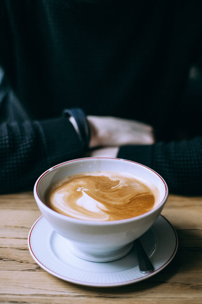 A single latte in a cup and saucer sits on a wooden table.