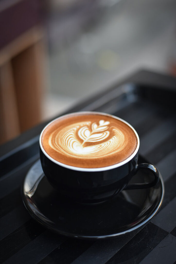 A single latte in a black mug sits on a black table representing healthy alternatives to sugar in coffee.