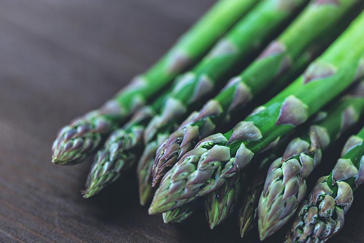 Spears of asparagus on a dark wood surface.