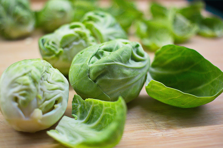 A few raw brussels sprouts sitting on a light wood surface.