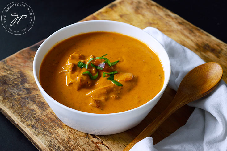 A white bowl filled with Butter Chicken. A wooden spoon lays next to the bowl on a white napkin.