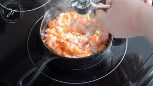 Pressing garlic into sautéing vegetables in a skillet on the stove.