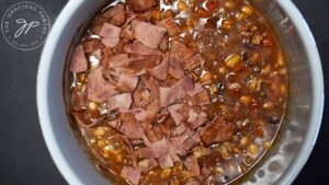 Chopped bacon added to all the other Cowboy Beans Recipe ingredients in a crock.