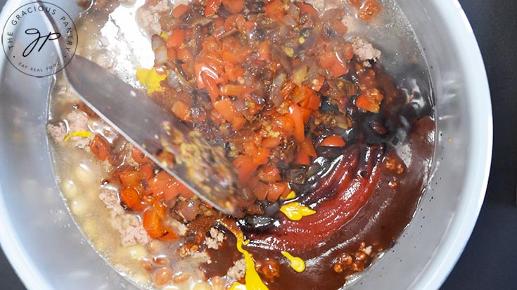 Stirring sautéd vegetables into Cowboy Beans ingredients in a crock.