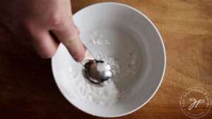 Adding water to arrowroot powder in a white bowl.
