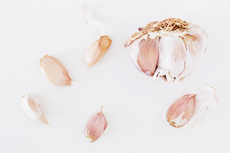 A broken up head of garlic on a white background.