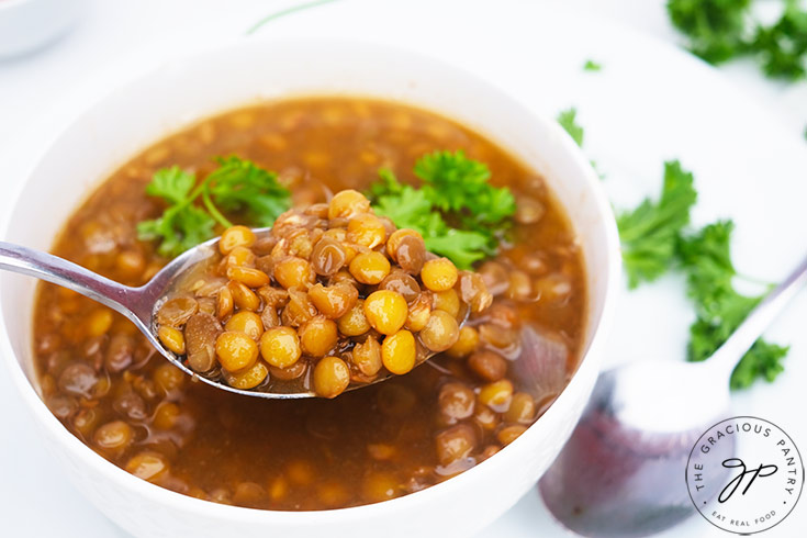 A spoon lifts some German Lentil Soup out of a white bowl.