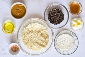 Individual bowls of Healthy Twix Bars Recipe ingredients on a white surface.