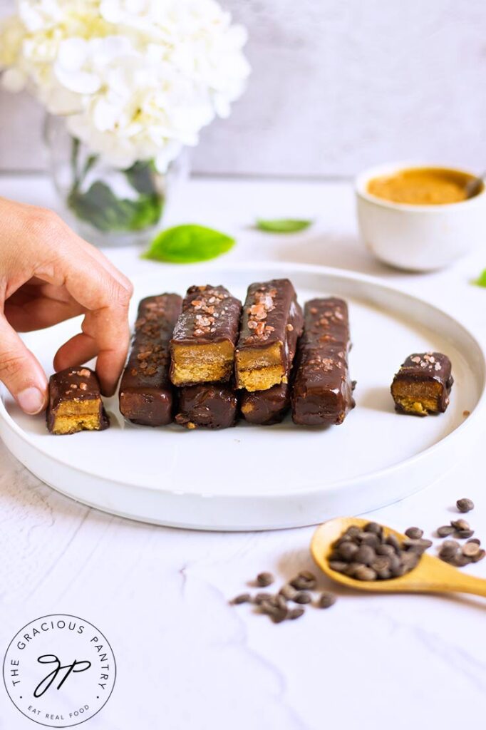 A female hand reaches for a Healthy Twix Bar from a stack on a white plate.