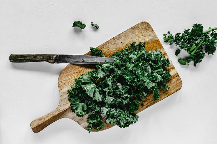 Chopped kale sitting on a cutting board with a knife, depicting kale as one of the items on this list of superfoods.