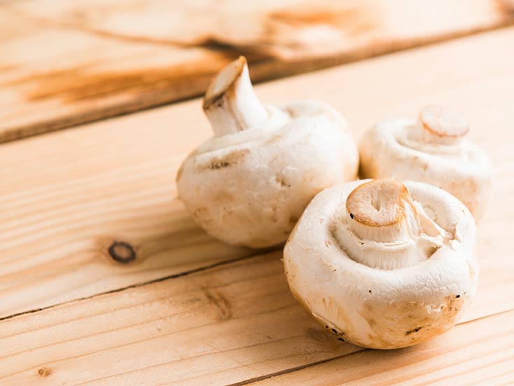 This list of superfoods includes mushrooms. This photo shows three white mushrooms, upside down on a wood surface.