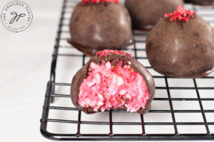 Just cooled Raspberry Coconut Truffles sitting on a cooling rack. The front truffle has a bite taken from it.