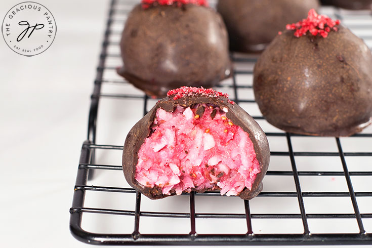 Just cooled Raspberry Coconut Truffles sitting on a cooling rack. The front truffle has a bite taken from it.