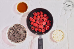 Raspberries in a small pot with bowls of chocolate chips, coconut and maple syrup sitting around it.