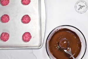 A fork pulls a Raspberry Coconut Truffle ball out of a bowl of melted chocolate.