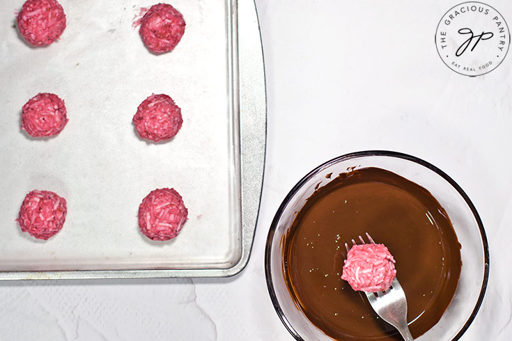 A fork dips a Raspberry Coconut Truffle ball into melted chocolate.