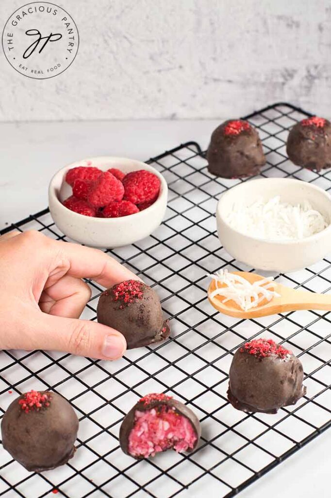 A female hand picks up a Raspberry Coconut Truffle off of a cooling rack.