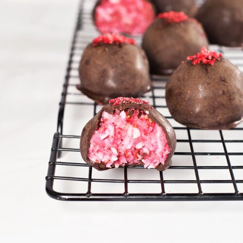 Raspberry Coconut Truffles sitting on a cooling rack, dusted with rapsberry powder.