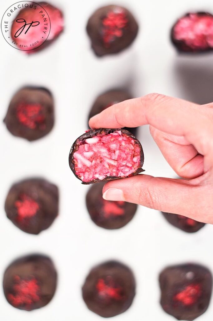 A female hand holds a have eated Raspberry Coconut Truffle.