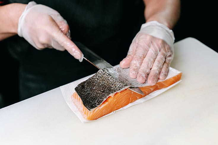 Skin being sliced off a raw salmon filet.