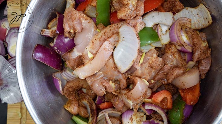 Chicken and veggies mixed togehter with spices in a mixing bowl.