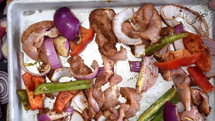 Uncooked, spiced chicken and veggies on a baking pan.