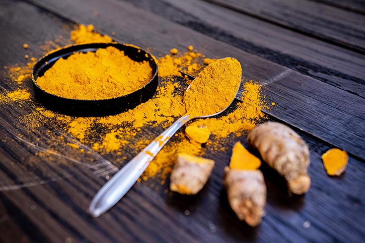 Ground turmeric in a shallow, black dish with a spoonful of it resting next to the dish, depicting turmeric as an item in this list of superfoods