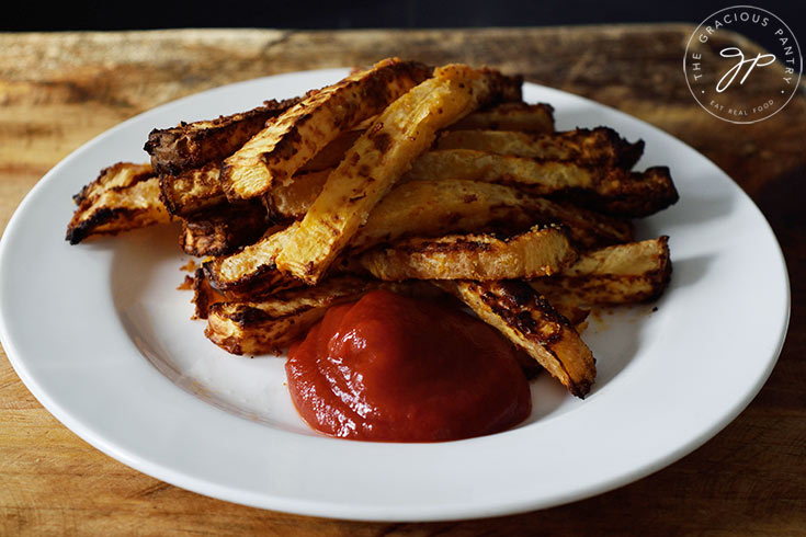 Just-cooked Air Fryer Rutabaga Fries laying on a white plate with some ketchup.