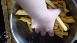 Tossing raw, but rutabaga fries in a mixing bowl.