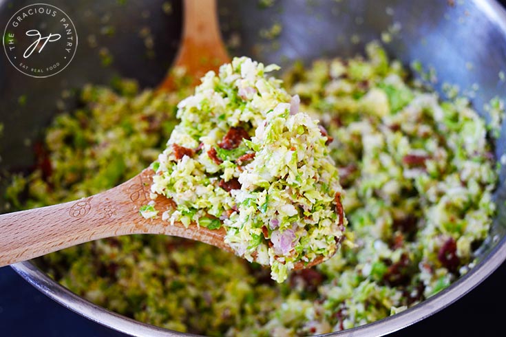 A wooden spoon holds up a spoonful of Brussels Sprouts Salad.