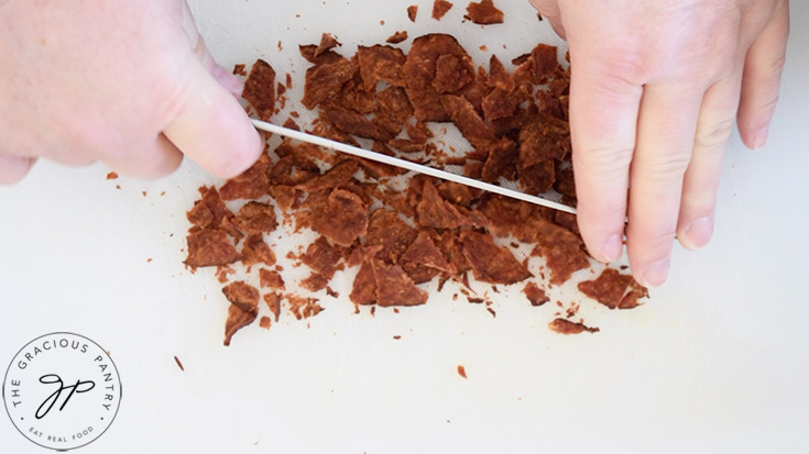 Chopping cooked bacon into bacon bits.