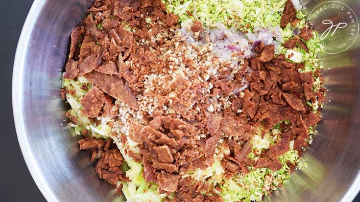 Bacon bits added to a mixing bowl of Brussels Sprouts Salad ingredients.