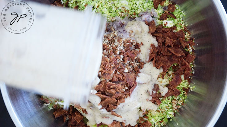 Pouring dressing over the salad ingredients in a mixing bowl.