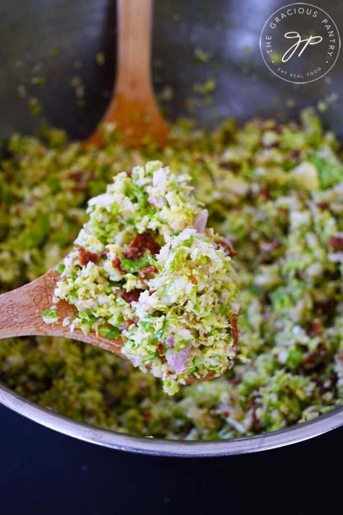 A closeup of a wooden spoon holding a spoonful of Brussels Sprouts Salad.