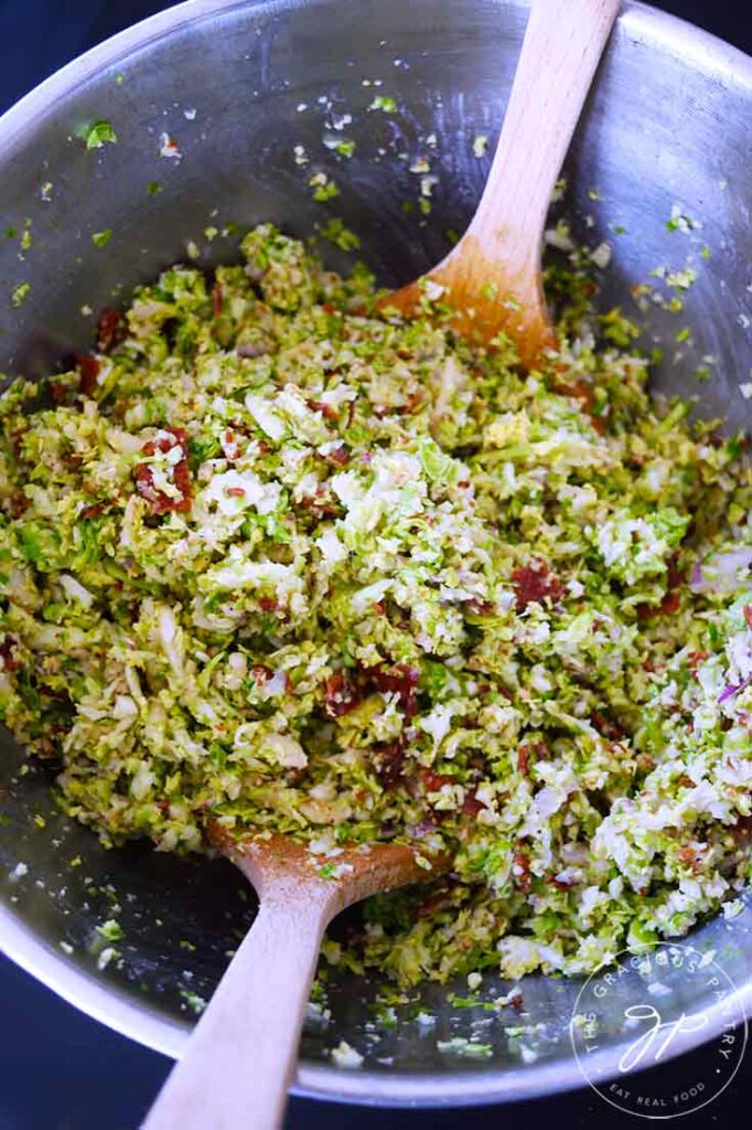 An overhead view of two wooden spoons inside a mixing bowl filled with Brussels Sprouts Salad.