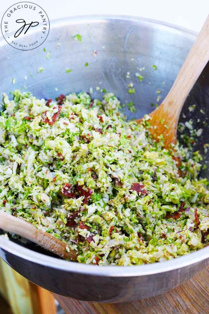 A side view of two wooden spoons resting in a bowl filled with Brussels Sprouts Salad.