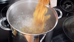 Pouring dry pasta into a pot of boiling water.