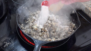Adding salt to mushrooms and garlic in a skillet.