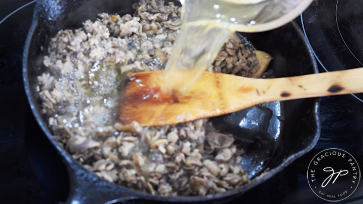 Adding chicken broth to mushrooms and garlic in a skillet.