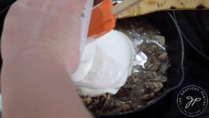 Adding yogurt to mushrooms and garlic in a skillet.