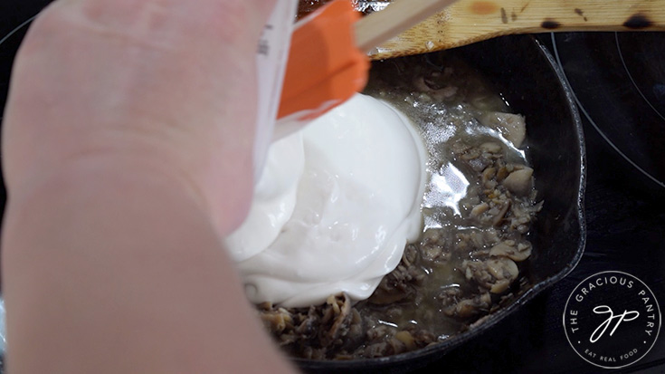 Adding yogurt to mushrooms and garlic in a skillet.
