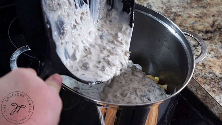 Pouring Creamy Garlic Mushroom Pasta sauce into a large pot of cooked pasta.