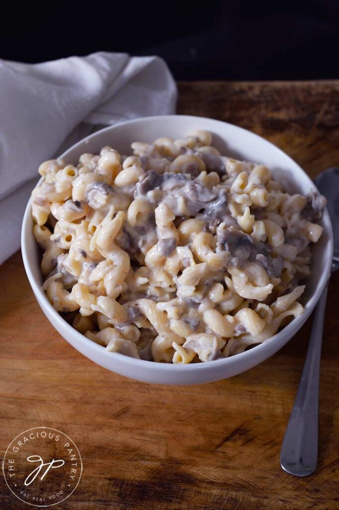 A white bowl filled with Creamy Garlic Mushroom Pasta sits on a wooden surface.