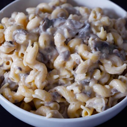 A white bowl on a black background sits filled with Creamy Garlic Mushroom Pasta.