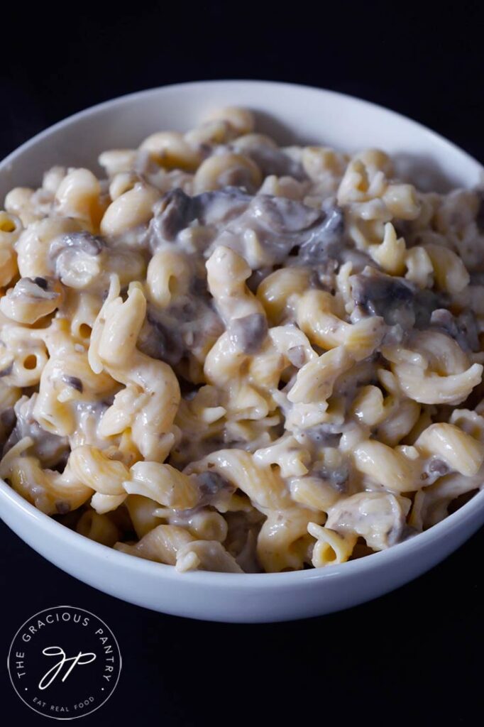 A white bowl on a black background sits filled with Creamy Garlic Mushroom Pasta.