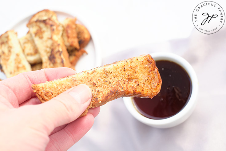 A female hand dips a French Toast Stick into a small cup of maple syrup.