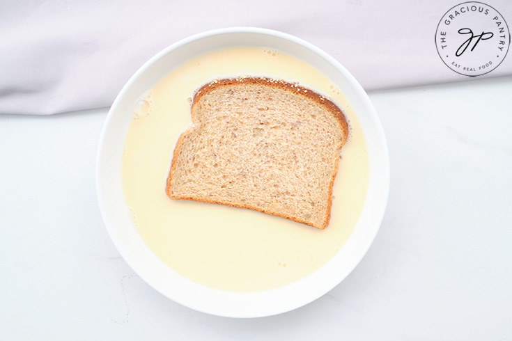 A slice of whole grain bread soaking in egg mixture.