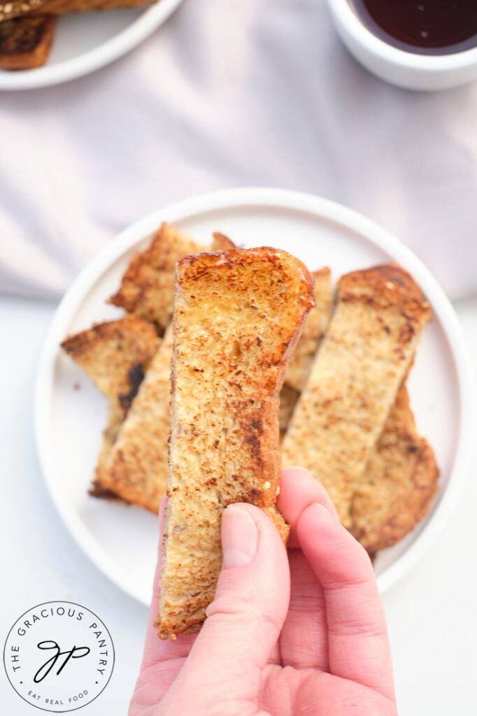 A female hand holds up a French Toast Stick.
