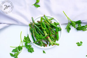 A white plate on a white background holds a serving of Garlicky Green Beans sprinkled with fresh parsley.